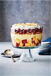 Cherry trifle in a glass trifle bowl with serving spoon on grey background