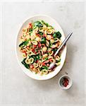 Platter of orecchiette pasta with peas, bacon, spinach and tomatoes and chili flakes in a small bowl on a beige background