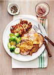 Roast pork with apple sauce, brussels sprouts and potato patties on a white plate with fork and knife