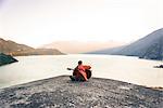 Young man sitting on The Malamute, playing guitar, rear view, Squamish, Canada