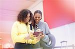 Two mid adult women looking at passports in airport departure lounge