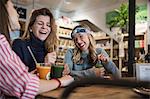 Three female friends, sitting in cafe, drinking smoothies, laughing