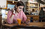 Young woman sitting in cafe, using smartphone, smoothie on table in front of her