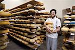 Portrait of cheese maker carrying hard cheeses for inspection, in ageing room where hard cheeses are stored