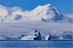 Non-tabular iceberg off glaciated, mountainous Anvers Island, blue sky, Antarctic Peninsula, Antarctica, Polar Regions