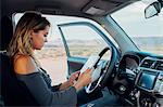 Young woman sitting in vehicle, looking at digital tablet, Mexican Hat, Utah, USA