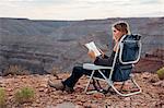 Young woman in remote setting, sitting on camping chair, reading book, Mexican Hat, Utah, USA