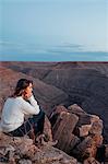 Young woman in remote setting, sitting on rocks, looking at view, Mexican Hat, Utah, USA