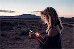 Young woman in remote setting, using smartphone, Mexican Hat, Utah, USA