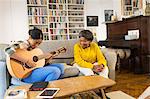 Grandmother watching granddaughter playing guitar on sofa