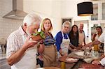 Active senior friends taking cooking class, smelling fresh basil