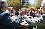 Active senior friends holding hands, praying at sunny garden party table