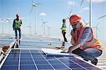 Engineer with walkie-talkie and blueprint at solar panel at sunny power plant
