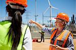 Female engineer with digital tablet talking to colleague at wind turbine power plant