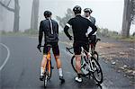 Male cyclist friends taking a break, resting on wet road