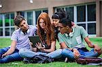 College students sitting on lawn looking at digital tablet together