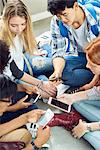 Group of students sitting together on floor, looking at smartphones