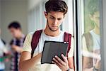 Male college student using digital tablet in corridor