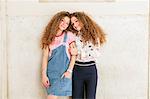 Fashion blogger twins leaning against wall
