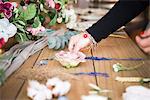 Woman arranging flower head and stems on wooden table, detail of hand