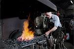 Blacksmith heating metal in forge fire in blacksmiths shop