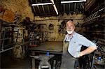 Blacksmith with hands on hips in blacksmiths shop, portrait