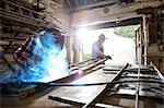 Senior blacksmith and son welding metal on workbench in blacksmiths shop