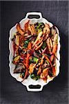 Roasted vegetables on a white platter on a dark linen tablecloth, black background