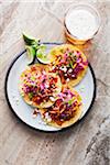 Chicken tacos on a plate with limes and a glass of beer