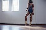 Graceful young female ballet dancer stretching foot in dance studio