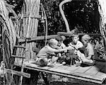 1950s 1960s FOUR BOYS IN TREE HOUSE CLUBHOUSE HOLDING HANDS OVER FAKE CAMPFIRE SWEARING TAKING OATH