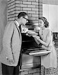 1950s COUPLE IN KITCHEN WOMAN SHOWING FRESHLY BAKED PIE TO MAN