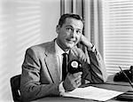 1950s WORRIED BUSINESSMAN SITTING AT DESK BEHIND BLACK EIGHT BALL LOOKING AT CAMERA