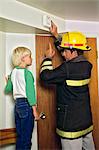 MAN FIREFIGHTER IN PROTECTIVE HELMET AND TURNOUT JACKET INSTRUCTING YOUNG BLOND BOY ABOUT HOME SMOKE DETECTOR FIRE ALARM