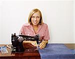 1970s WOMAN OPERATING SEWING MACHINE HOUSEHOLD APPLIANCE SEW SKILL CRAFT HOUSEWIFE WEARING CHECKED BLOUSE LOOKING AT CAMERA