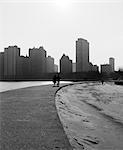 1960s TWO ANONYMOUS SILHOUETTED PEOPLE WALKING ALONG LAKE SHORE CHICAGO ILLINOIS USA