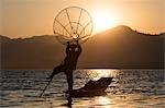 A fisherman standing on one leg and holding his fishing net at sunset on Inle Lake, Shan State, Myanmar (Burma), Asia