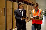 Worker and businessman with digital tablet and clipboard in warehouse