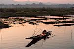 A fisherman keeps warm in his long tail fishing boat at dawn near the floating gardens on Inle Lake, Shan State, Myanmar (Burma), Asia