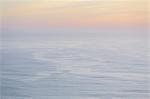 The open ocean, water surface calm and grey and the glow of the sun at dawn on the horizon.