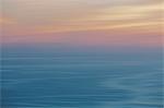View out to sea over the ocean at dusk,  the sunset light on the horizon and calm undulating sea surface. Abstract coloured light effect.
