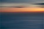 View out to sea over the ocean at dusk,  the sunset light on the horizon and calm undulating sea surface. Abstract coloured light effect.