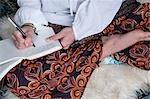 High angle view of woman wearing trousers with floral pattern sitting on shag carpet, writing in diary.