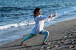 Young woman with brown hair wearing white blouse standing on a beach by the ocean, doing Tai Chi.