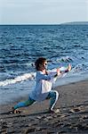 Young woman with brown hair wearing white blouse standing on a beach by the ocean, doing Tai Chi.