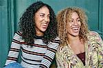 Portrait of two young smiling women with long curly black and blond hair, smiling and laughing.