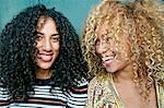 Portrait of two young women with long curly black and blond hair, smiling at camera.