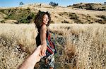 Young woman with curly brown hair hiking in urban park, holding man's hand.