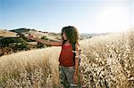 Young woman with curly brown hair hiking in urban park, taking picture with mobile phone.