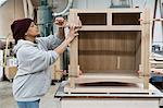 A Black woman carpenter working on a cabinet project in a large woodworking shop.